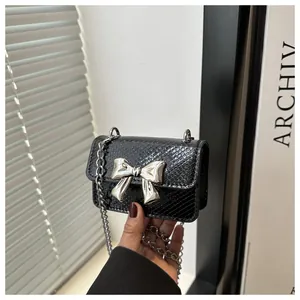 Detailed view of black snake-embossed mini bag with silver metal bow and chain strap