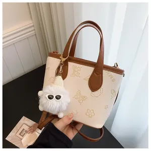 Close-up of cream PU leather bucket bag with embossed patterns and plush charm