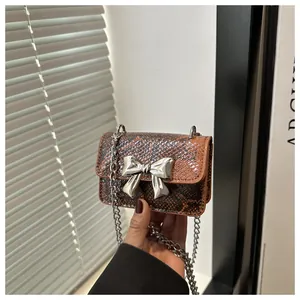 Close-up of brown snake print mini bag featuring a silver metal bow and chain strap