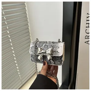 Detailed view of snake skin texture and silver bow buckle on mini chain shoulder bag