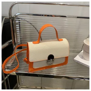 Detail of a bright orange leather handbag with white woven flap and silver buckle lock