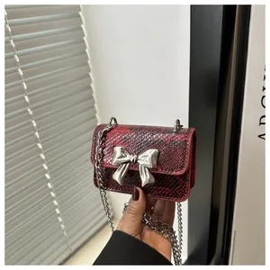 Close-up of a mini red and black snakeskin leather bag with silver bow hardware and chain