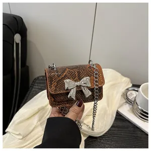 Detail of snake skin texture mini bag with silver bow buckle and metal chain strap