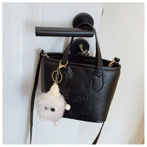 Close-up of black bucket bag with cartoon embossing and a white plush monster charm