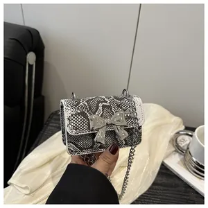 Close-up of mini snakeskin crossbody bag featuring a large silver metallic bow accent