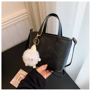 Detail of black embossed leather handbag featuring floral patterns and a cute plush charm
