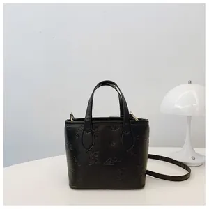 Detail view of the embossed floral patterns and golden hardware on the black leather bucket bag