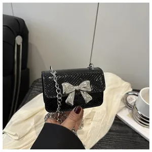 Detail of black snake-textured mini bag with silver bow buckle and chain strap