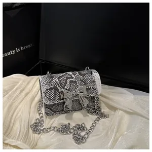 Detail of snake print mini bag with silver bow clasp and elegant chain strap