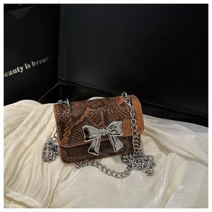 Macro detail of brown snakeskin crossbody bag with a large silver bow and metal chain strap