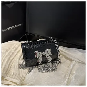 Macro shot of silver bow detail and snake pattern texture on black mini chain bag