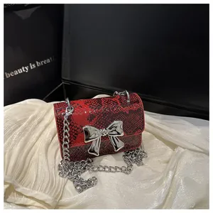 Close-up of red snakeskin mini bag with silver bow ornament on white silk fabric