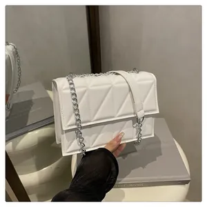 Detail of white quilted rectangle crossbody bag with silver chain strap on soft surface