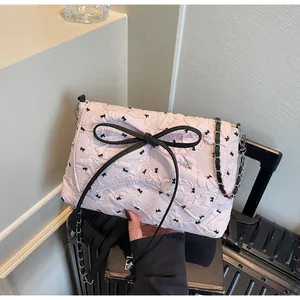 Detail der rosa Schultertasche aus Knitterstoff mit schwarzem Schleifenmuster und Kettenriemen