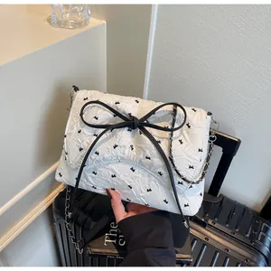 Detailansicht der weißen Stepptasche mit schwarzen Schleifen und Metallkettenriemen