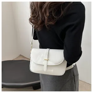 Detail of white patent leather shoulder bag with gold hardware shown on a model