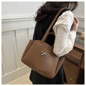 Fashionable caramel tote bag with silver metal bow worn by model in a stylish interior