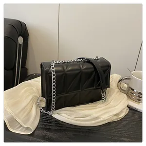 Detail of black geometric quilted crossbody bag with silver chain on elegant white fabric