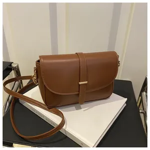 Close-up of brown leather crossbody bag with gold metal buckle on minimalist book