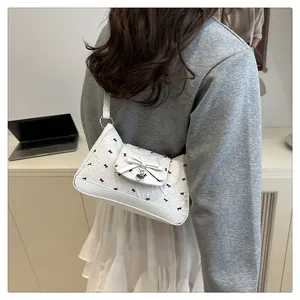 Détail d'un sac à bandoulière blanc avec broderie nœud, pendentif cœur et texture
