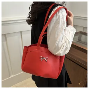 Detailed view of red matte leather tote bag featuring a silver metal bow accessory