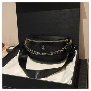 Close-up of black leather crossbody bag with skull embossing and gold chain in gift box
