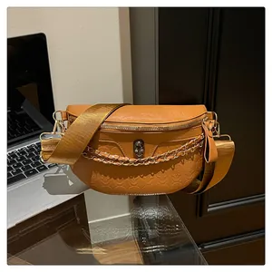 Detail of tan skull embossed leather chest bag with metal skull charm and gold chain