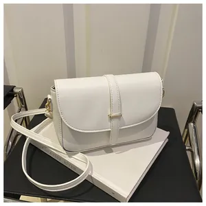 Detail of white leather shoulder bag with golden buckle on minimalist book stand
