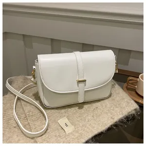 Close-up of elegant white leather handbag with golden hardware on a soft beige fabric
