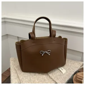 Detail of a brown leather tote bag featuring a silver metal bow accent and dual handles