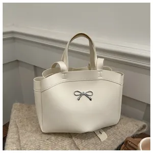 Close-up of cream white tote bag featuring a decorative silver metal bow and dual handles