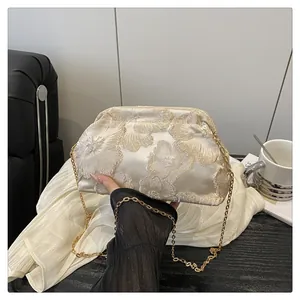 Detailed shot of beige cosmetic bag with gold flower embroidery and delicate metal chain