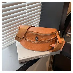 Detail of caramel half-moon bag featuring skull embossing and decorative metal chains