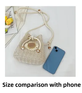 Detail of straw bucket bag showing daisy decor and size comparison with a smartphone