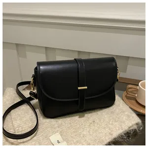 Detail of a minimalist black leather crossbody bag with a gold metal bar buckle on fabric