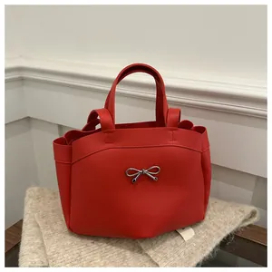 Detail of red faux leather tote bag featuring a silver metal bow accent on beige scarf