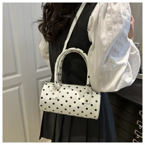 Close-up of a mini polka dot cylinder bag with black handles and metal zipper detail