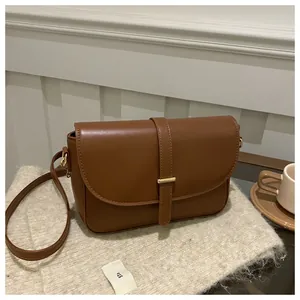 Close-up of brown leather saddle bag with gold buckle detail on soft beige fabric