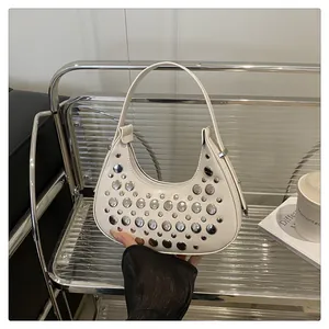 Close-up of white leather crescent bag featuring metallic silver studs and smooth texture