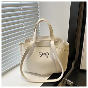 Detailed view of white leather tote bag with silver bow accent and shoulder strap