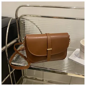 Brown vintage style leather crossbody bag with gold buckle on a stylish metal shelf