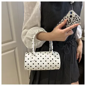 Chic polka dot cylinder handbag shown as cross-body style with sleek metal zipper detail