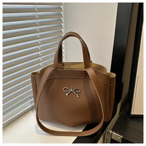Detail of a brown tote bag featuring a silver metal bow accent and smooth PU texture