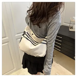 Détail du sac bandoulière en toile avec rayures noires et boucle métallique sur tissu