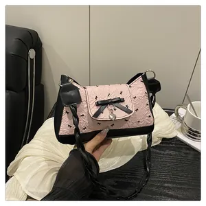 Détail du tissu plissé rose avec motifs nœuds noirs et pendentif cœur sur le sac à bandoulière
