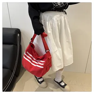 Détail du sac à bandoulière en toile rouge avec trois rayures blanches et sangle