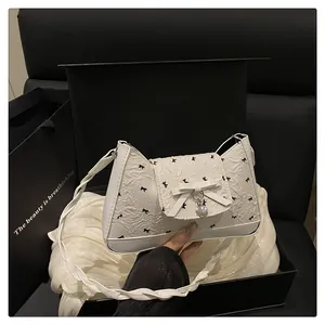 Détail du sac blanc texturé avec imprimés nœuds noirs et pendentif en forme de cœur