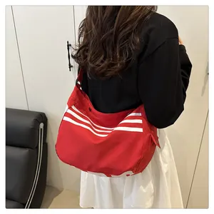 Détail d'un grand sac bandoulière rouge avec rayures blanches porté par une personne