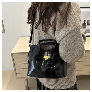 Detail of glossy black PU leather tote with golden triangular metal plaque and thin shoulder strap