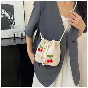 Detail of hand-woven beige straw bucket bag featuring 3D cherry poms and drawstring closure